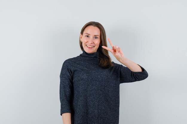 Young lady showing victory gesture in casual shirt and looking glad 