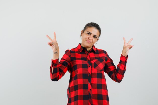 Young lady showing victory gesture in checked shirt and looking confident. 