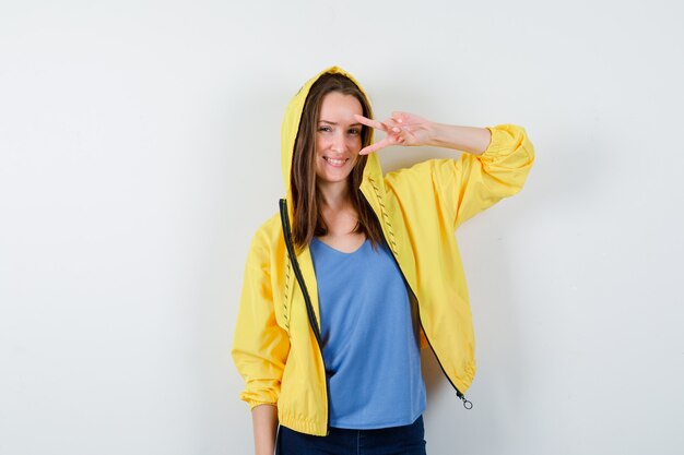 Young lady showing victory gesture near eye in t-shirt, jacket and looking confident , front view.