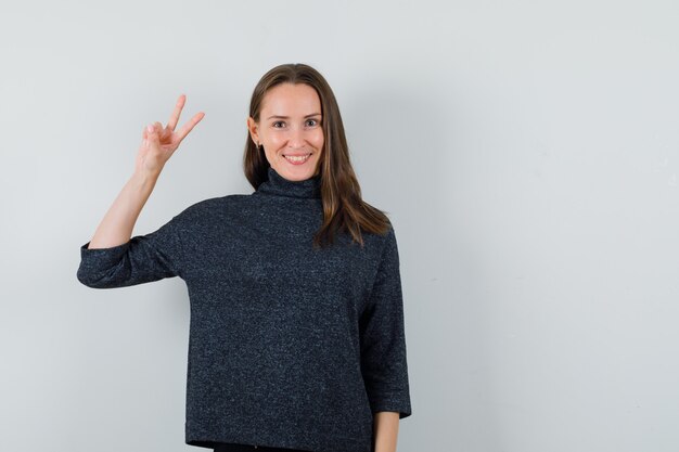 Young lady showing victory gesture in shirt and looking happy