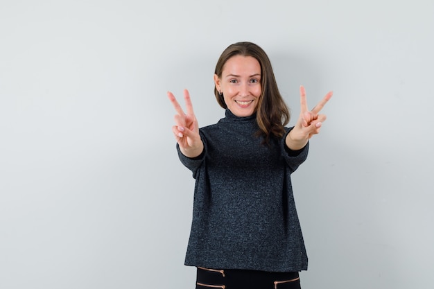 Free photo young lady showing victory gesture in shirt and looking merry