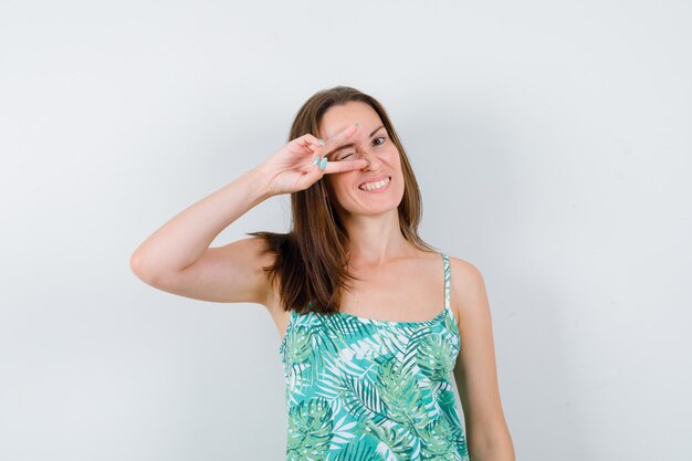 Young lady showing victory sign in blouse and looking blissful. front view.