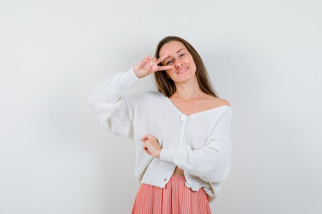 Young lady showing victory sign in cardigan and skirt looking blissful isolated