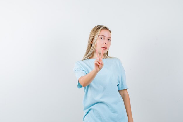 Young lady showing victory sign in t-shirt and looking lucky , front view.