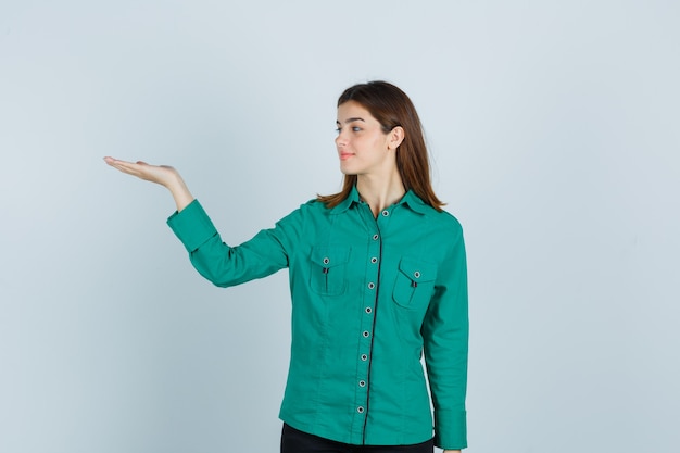 Young lady showing welcoming gesture in green shirt and looking cheerful , front view.