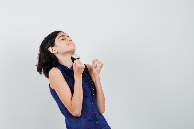 Young lady showing winner gesture in blouse and looking happy.