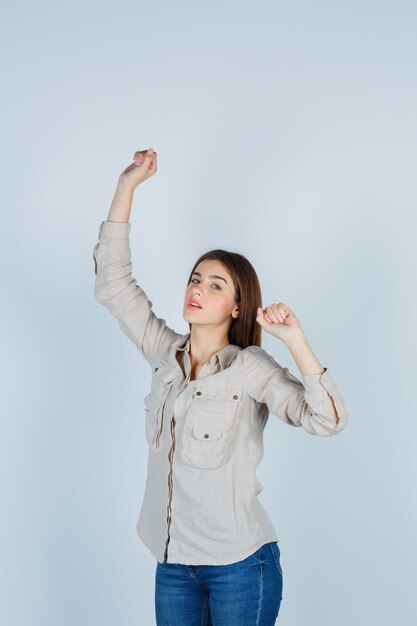 Young lady showing winner gesture in casual, jeans and looking successful , front view.