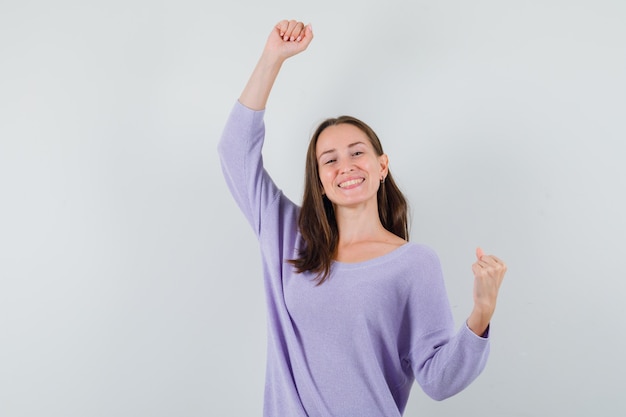 Young lady showing winner gesture in casual shirt and looking happy. front view.