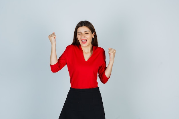 Free photo young lady showing winner gesture in red blouse, black skirt and looking lucky