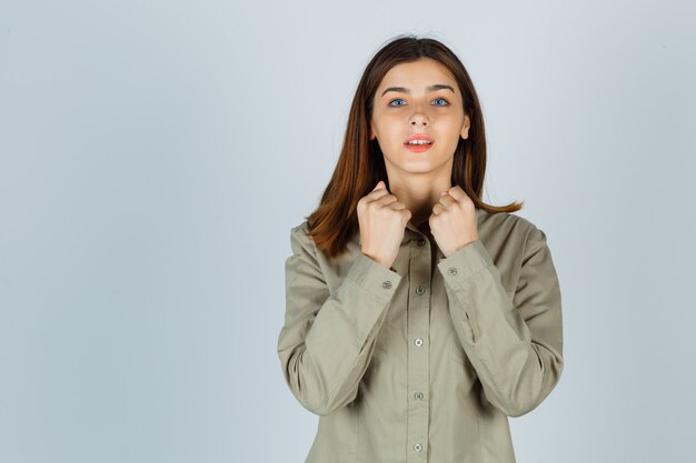 Young lady showing winner gesture in shirt and looking lucky , front view.