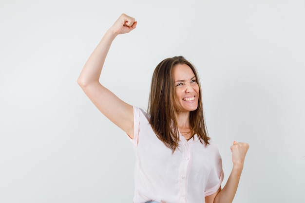 Tシャツで勝者のジェスチャーを示して幸せそうに見える若い女性。正面図。