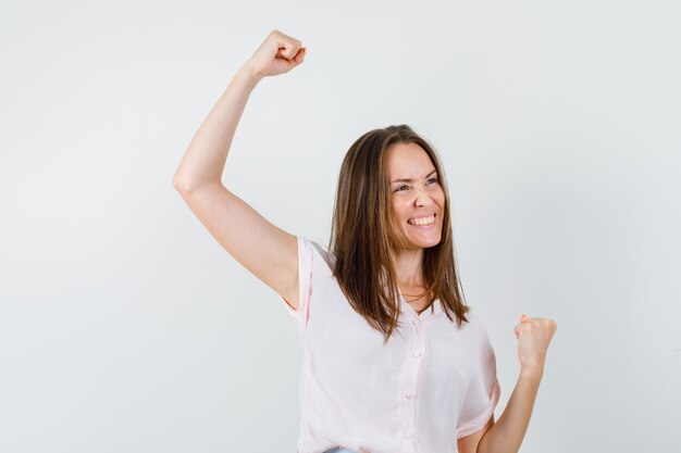 Young lady showing winner gesture in t-shirt and looking happy. front view.