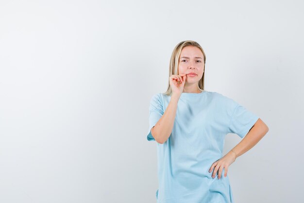 Young lady showing zip gesture while keeping hand on hip in t-shirt isolated