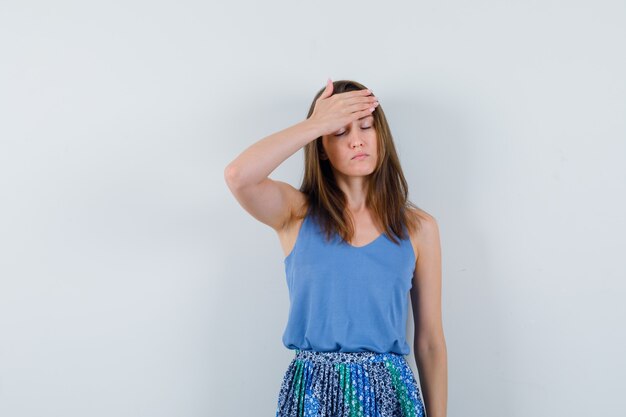 Young lady in singlet, skirt holding hand on forehead and looking tired