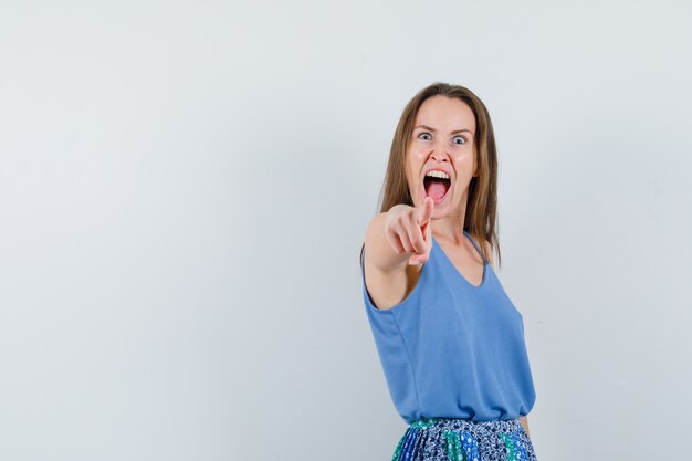 Young lady in singlet, skirt pointing at camera and looking aggressive , front view.