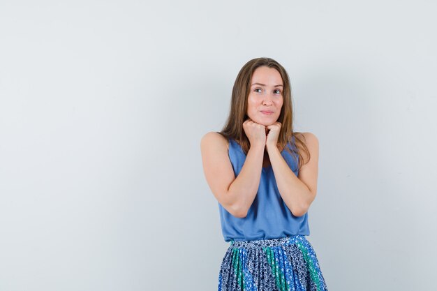 Young lady in singlet, skirt propping chin on fists and looking dreamy , front view.