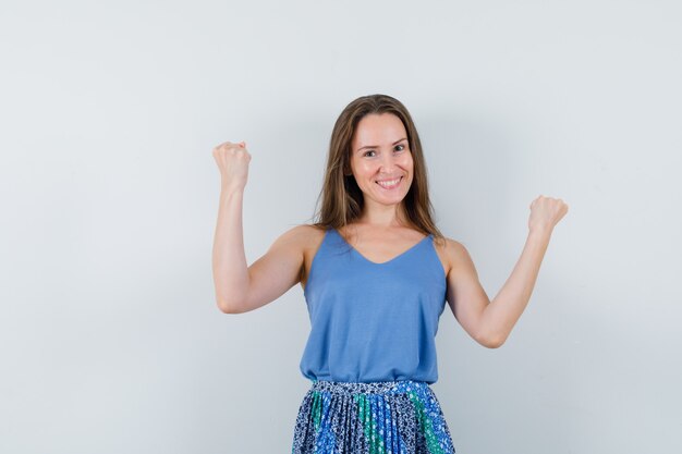 Young lady in singlet, skirt showing winner gesture and looking lucky , front view.