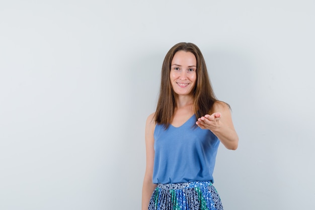 Young lady in singlet, skirt stretching hand and looking cheerful