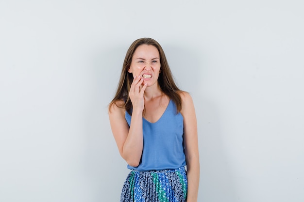 Young lady in singlet, skirt suffering from toothache and looking uncomfortable