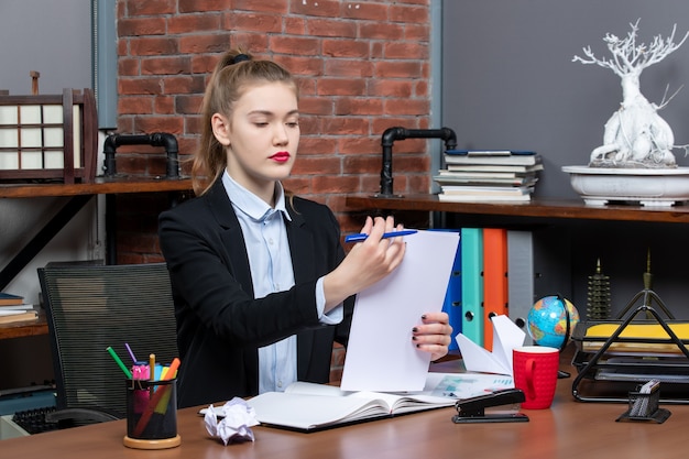 Free photo young lady sitting at a table and reading her notes in notebook in the office