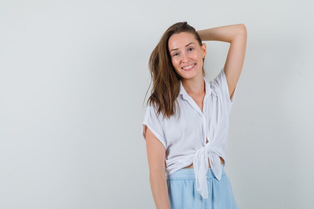 Young lady smiling while posing with hand on head in blouse, skirt and looking positive