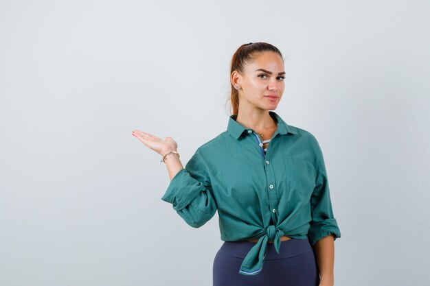 Young lady spreading palm aside in green shirt and looking confident. front view.