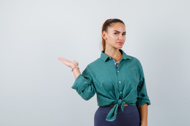 Young lady spreading palm aside in green shirt and looking confident. front view.