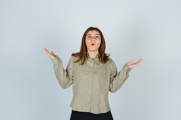 Giovane donna che allarga le palme da parte in camicia, gonna e sembra perplessa