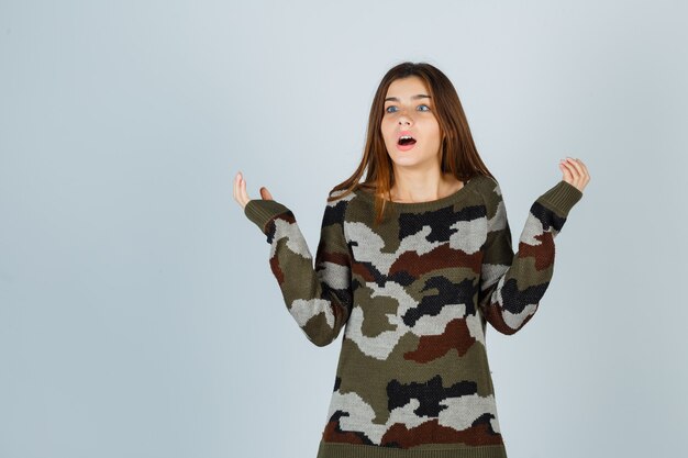 Young lady spreading palms aside in sweater and looking perplexed