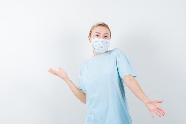 Free photo young lady spreading palms aside in t-shirt, mask and looking careful