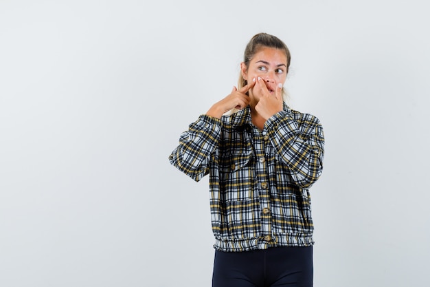 Young lady squeezing her pimple on cheek in shirt, shorts , front view.