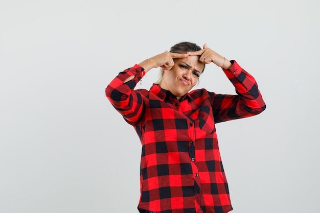 Free photo young lady squeezing her pimple on forehead in checked shirt