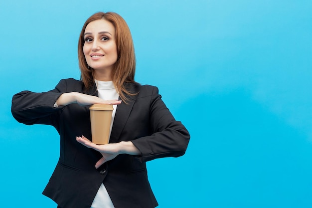 Девушка стоит на синем фоне и держит чашку кофе обеими руками