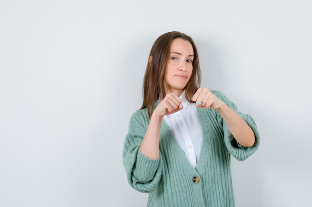 Young lady standing in fight pose in shirt, cardigan and looking confident , front view.