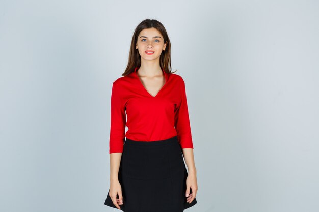 young lady standing straight while posingin red blouse, black skirt and looking cheery