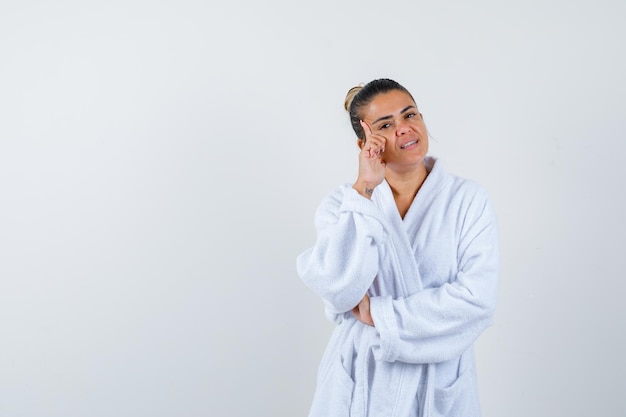 Young lady standing in thinking pose in bathrobe and looking thoughtful