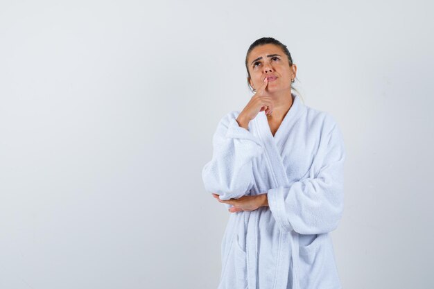 Young lady standing in thinking pose in bathrobe and looking thoughtful