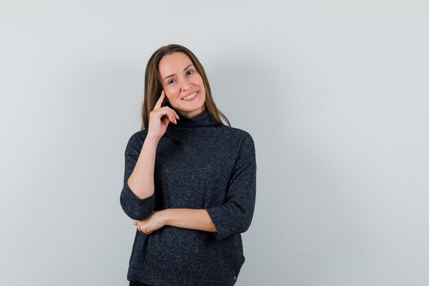 Young lady standing in thinking pose in casual shirt and looking merry. front view.