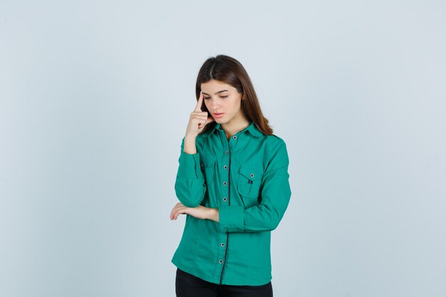 Девушка стояла в позе мышления в зеленой рубашке и выглядела обеспокоенной. передний план.