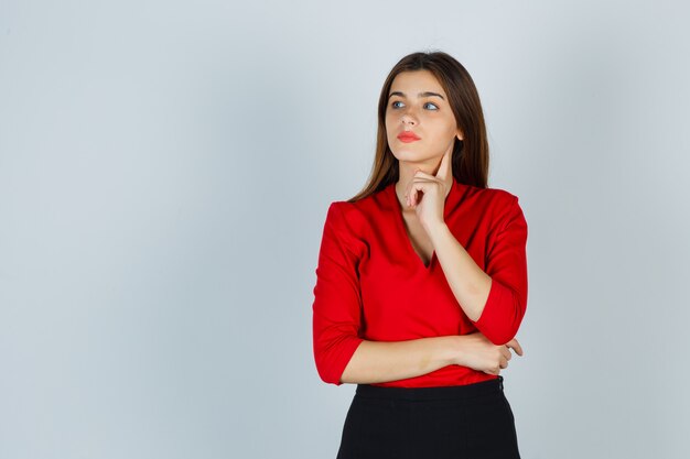young lady standing in thinking pose in red blouse, skirt and looking pensive
