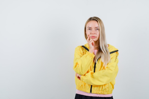 Young lady standing in thinking pose in t-shirt, jacket and looking pensive