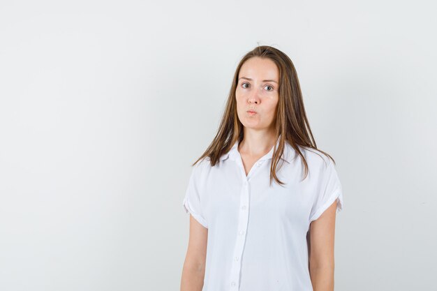 Young lady standing while pouting her lips in white blouse and looking serious