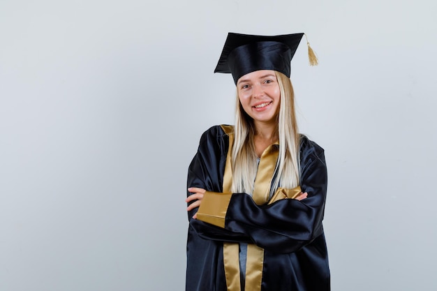 Young lady standing with crossed arms in academic dress and looking happy