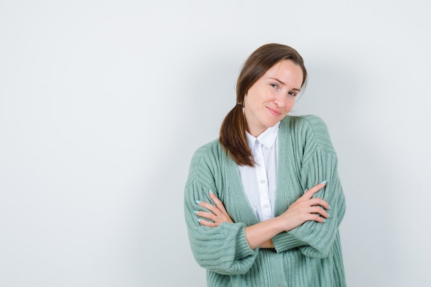 Young lady standing with crossed arms in blouse, cardigan and looking ashamed. front view.