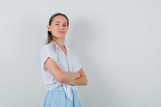 Young lady standing with crossed arms in blouse and skirt and looking confident