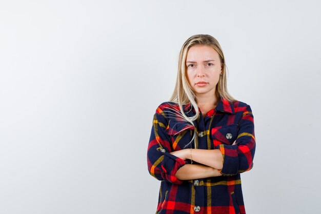 Young lady standing with crossed arms in checked shirt and looking confident. front view.