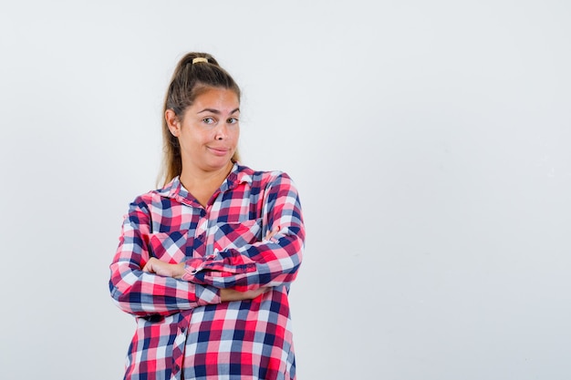 Young lady standing with crossed arms in checked shirt and looking proud. front view.