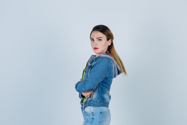 Young lady standing with crossed arms in denim outfit and looking .