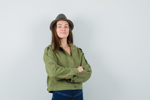 Young lady standing with crossed arms in jacket pants hat and looking confident 