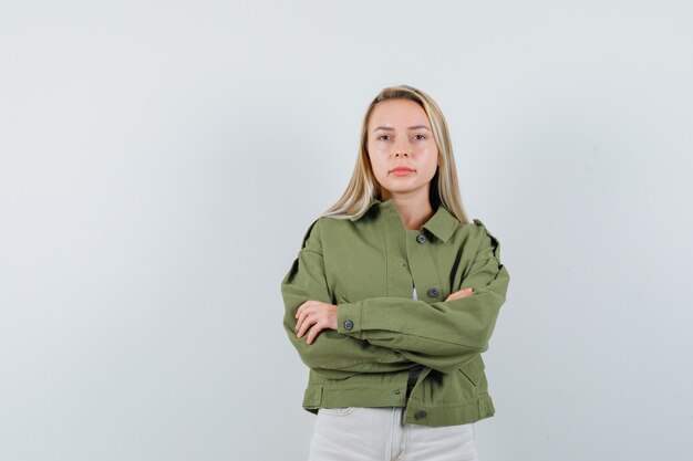 Young lady standing with crossed arms in jacket, pants and looking serious. front view.